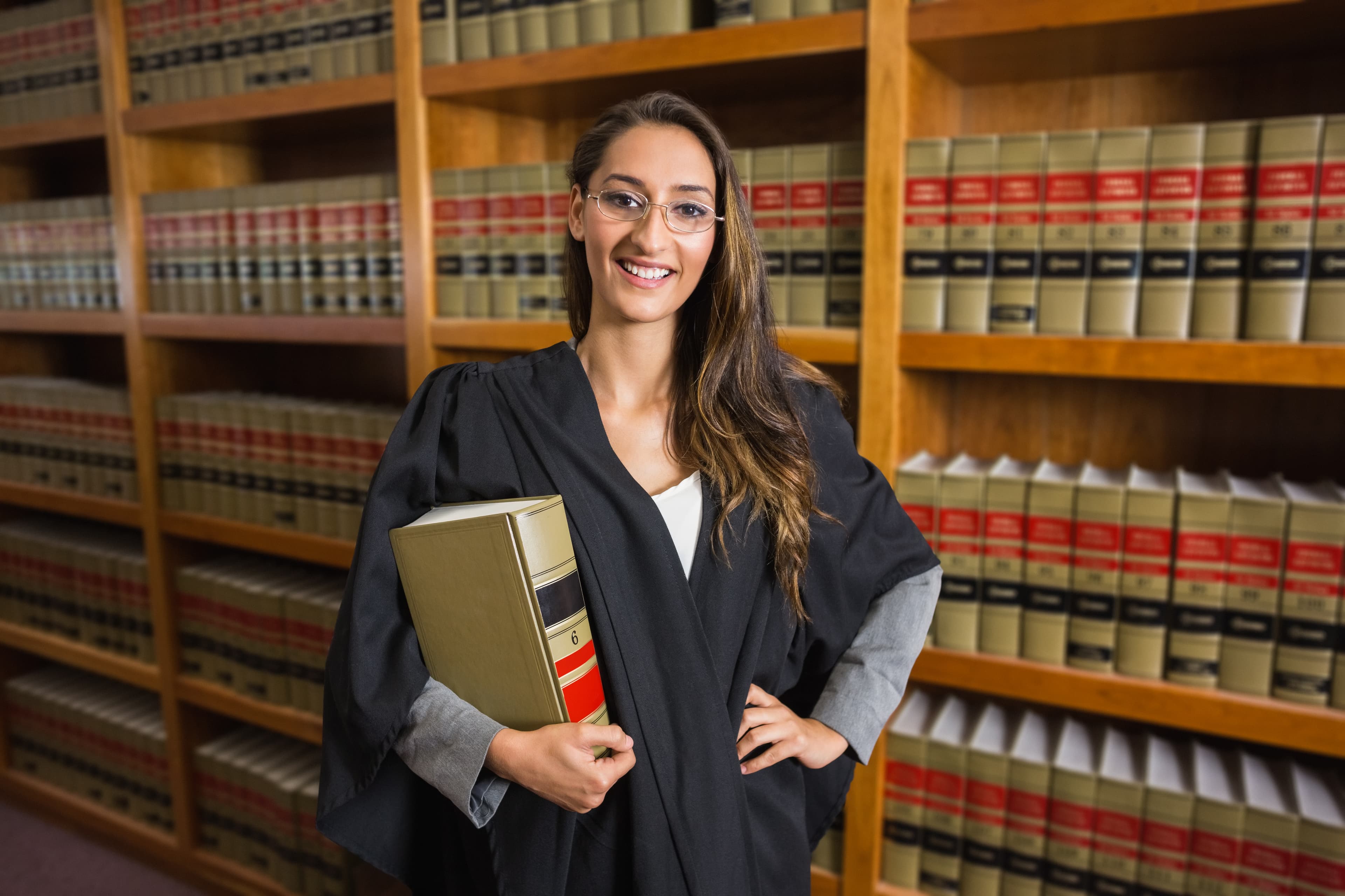 Law student smiling with a casebook in a law library