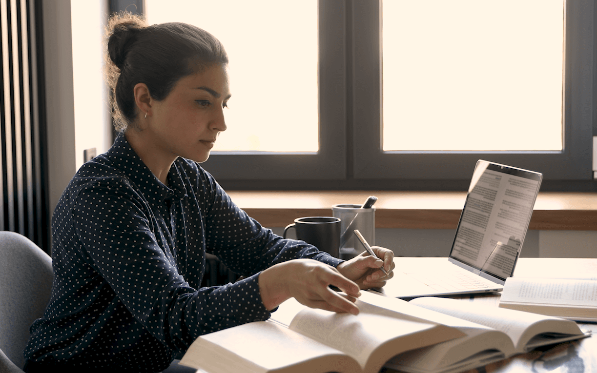 A student studying from an open textbook with a laptop open beside him