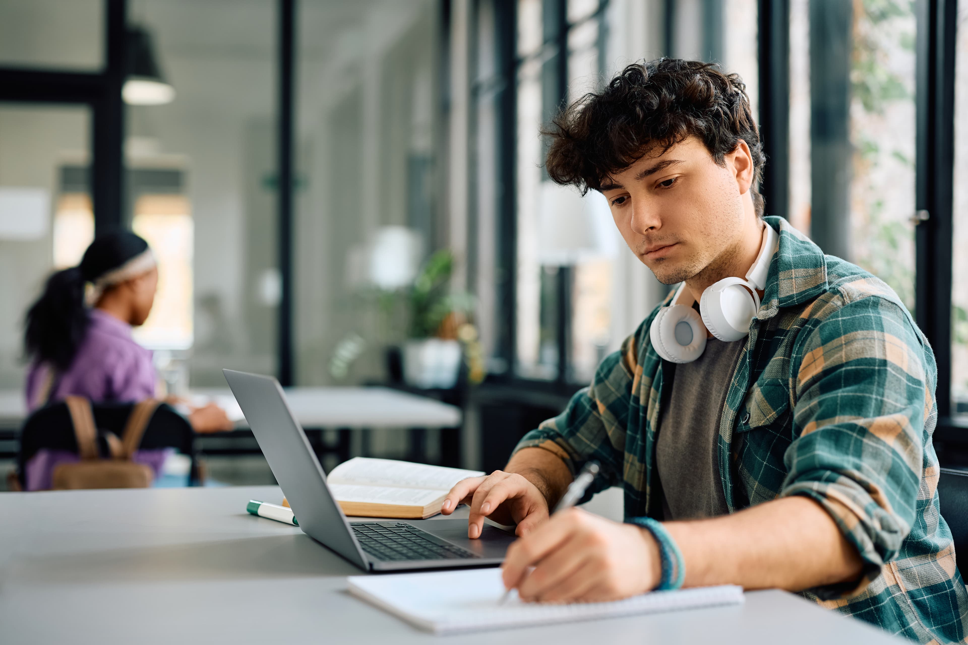 A student writing in a notebook beside an open laptop and textbook